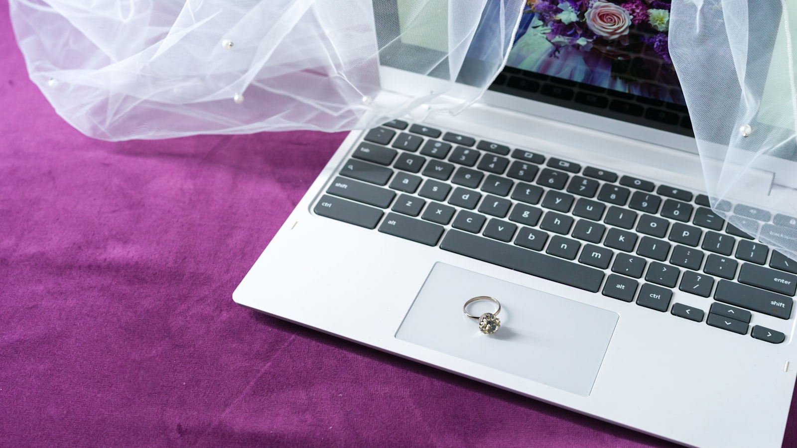 Overhead view of a wedding planning workspace with a laptop, an open planning notebook, and a bridal veil
