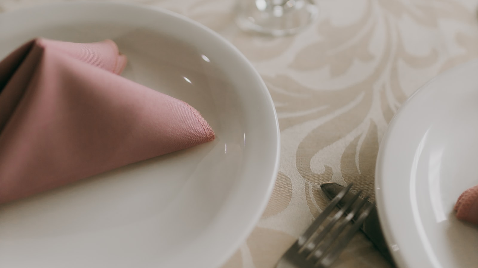Close-up of an elegant wedding place setting with white plates, polished silverware, and stemmed glassware on a linen-draped table