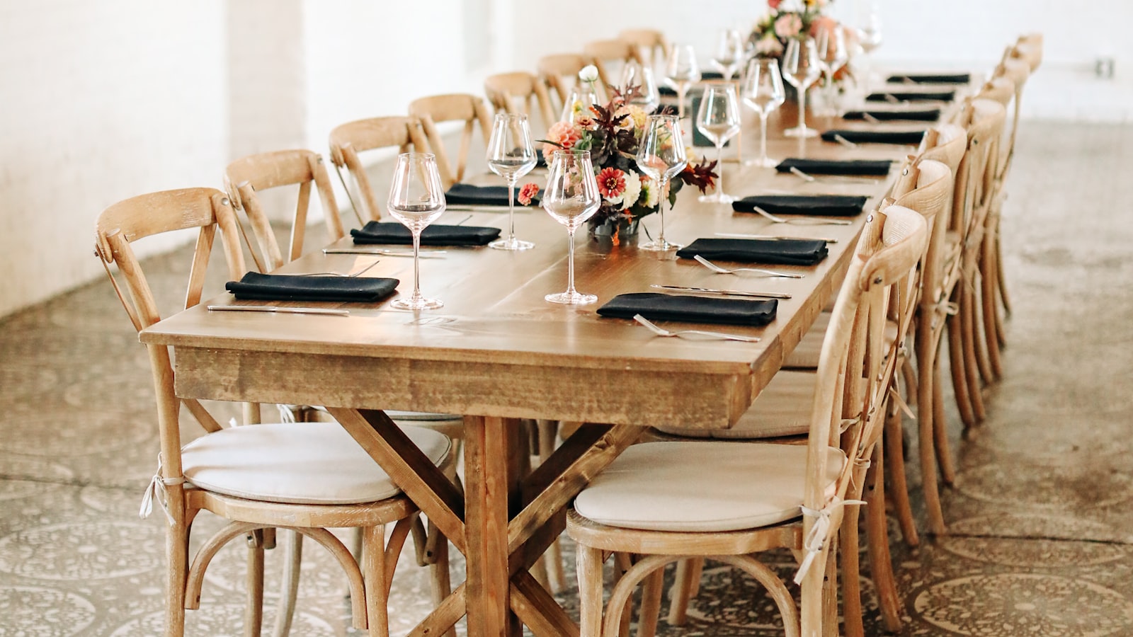 A long wooden banquet table set with chairs, place settings, and centerpieces, ready for a wedding head table