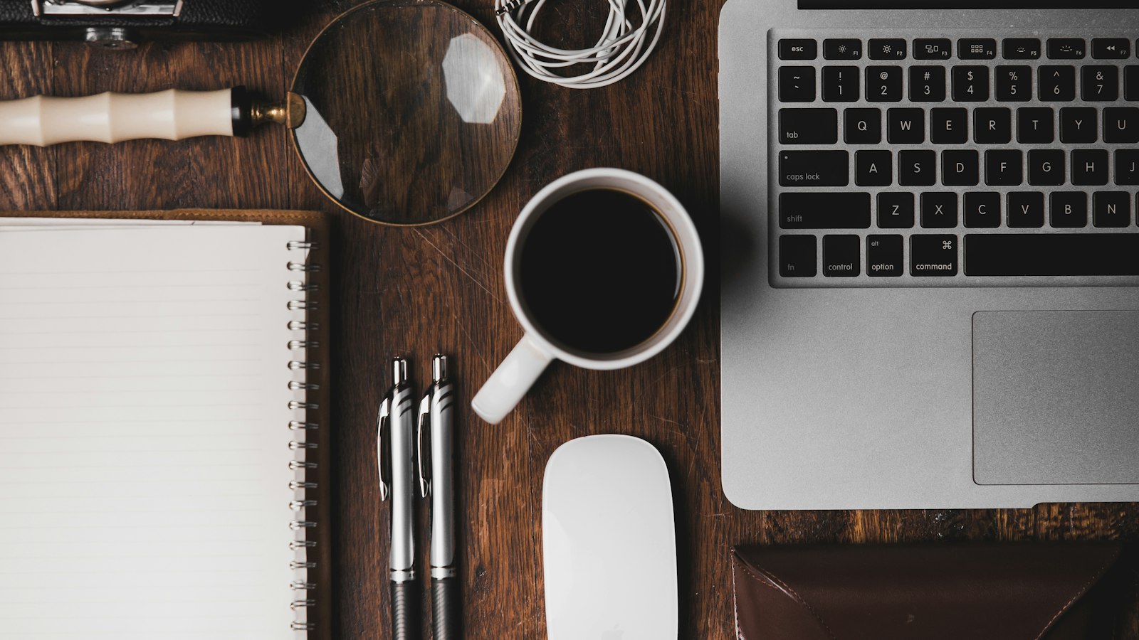 Overhead view of a planning desk with a laptop keyboard, open notebook, pens, and a cup of coffee